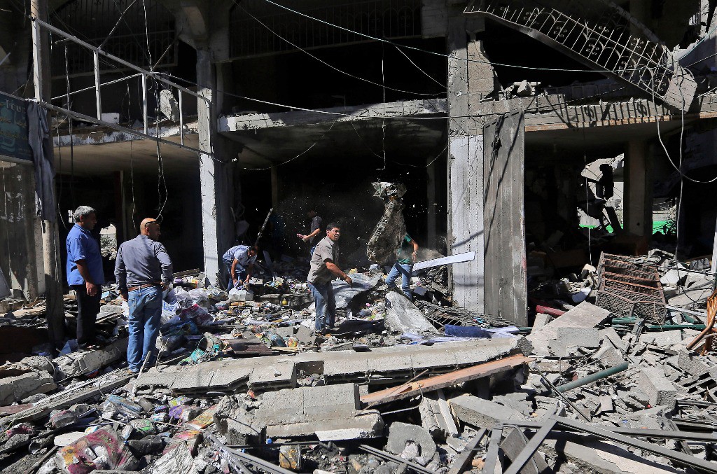 Palestinos inspeccionan entre los escombros de un edificio destruido en un ataque aéreo israelí en Gaza. Foto Ap