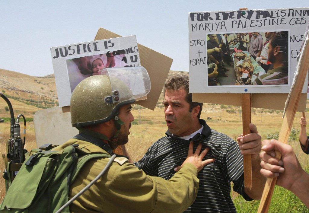 Un palestino muestra imágenes de víctimas frente a un soldado israelí en Gaza. Foto Reuters
