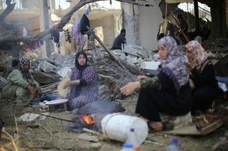 Mujeres palestinas hornean pan este jueves delante de los restos de su casa destruida en Khan Younis. Foto Reuters
