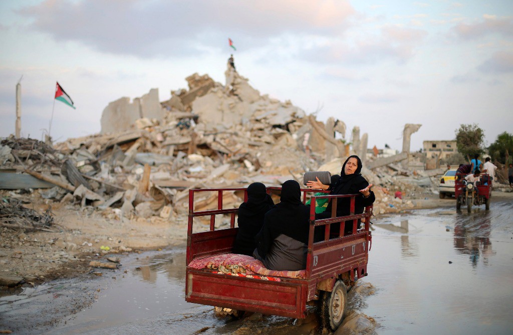 Palestinas se trasladan en el vagón de una motoneta adaptada, mientras atraviesan las ruinas de un hogar en la franja de Gaza. Foto Reuters