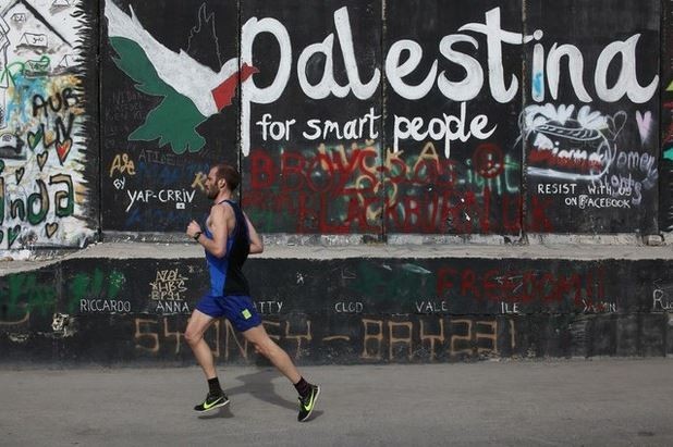 Un corredor pasa junto a una barda israelí, durante el tercer Maratón Internacional de Palestina, en Cisjordania. Foto Xinhua