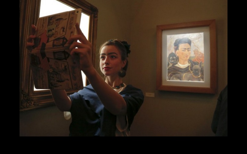 Una visitante caracterizada como Frida Kahlo se toma una 'selfie' junto a uno de los autorretratos de la mexicana en San Petersburgo. Foto Ap