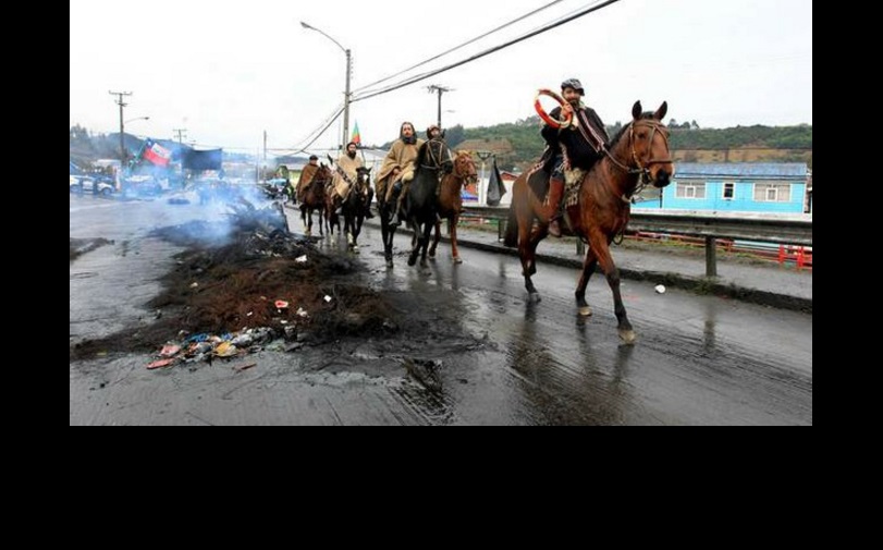 Pobladores del archipiélago de Chiloé cabalgan al lado de una barricada quemada. Foto Afp