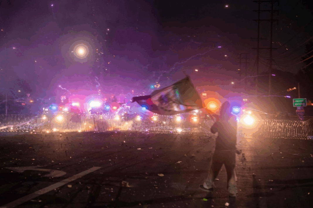 Una persona ondea la bandera mexicana mientras las fuerzas del orden se enfrentan con manifestantes durante una protesta tras las redadas federales de inmigración, en el barrio de Compton, Los Ángeles, California.